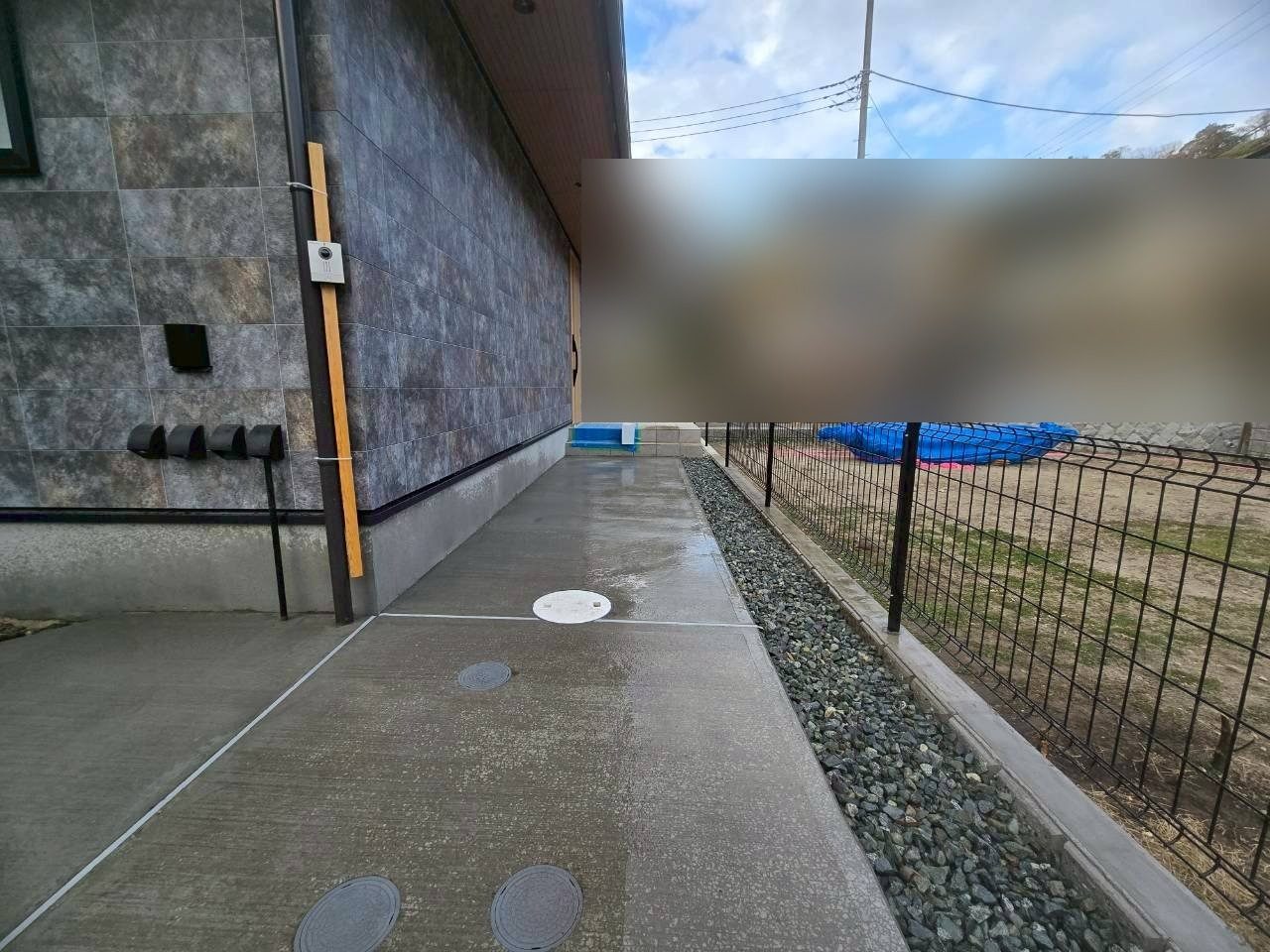 建物の横は土間コンクリートと砂利、黒のフェンスで